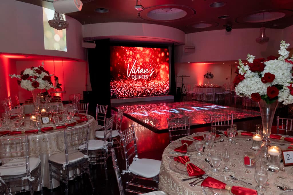 Elegante salón de recepción para quinceañera decorado con flores blancas y rojas y luces rojas